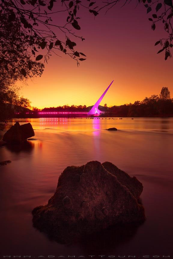 The Sundial Bridge in Redding, CA lit up pink for breast cancer awareness. Image taken at sunset with Sacramento River in foreground